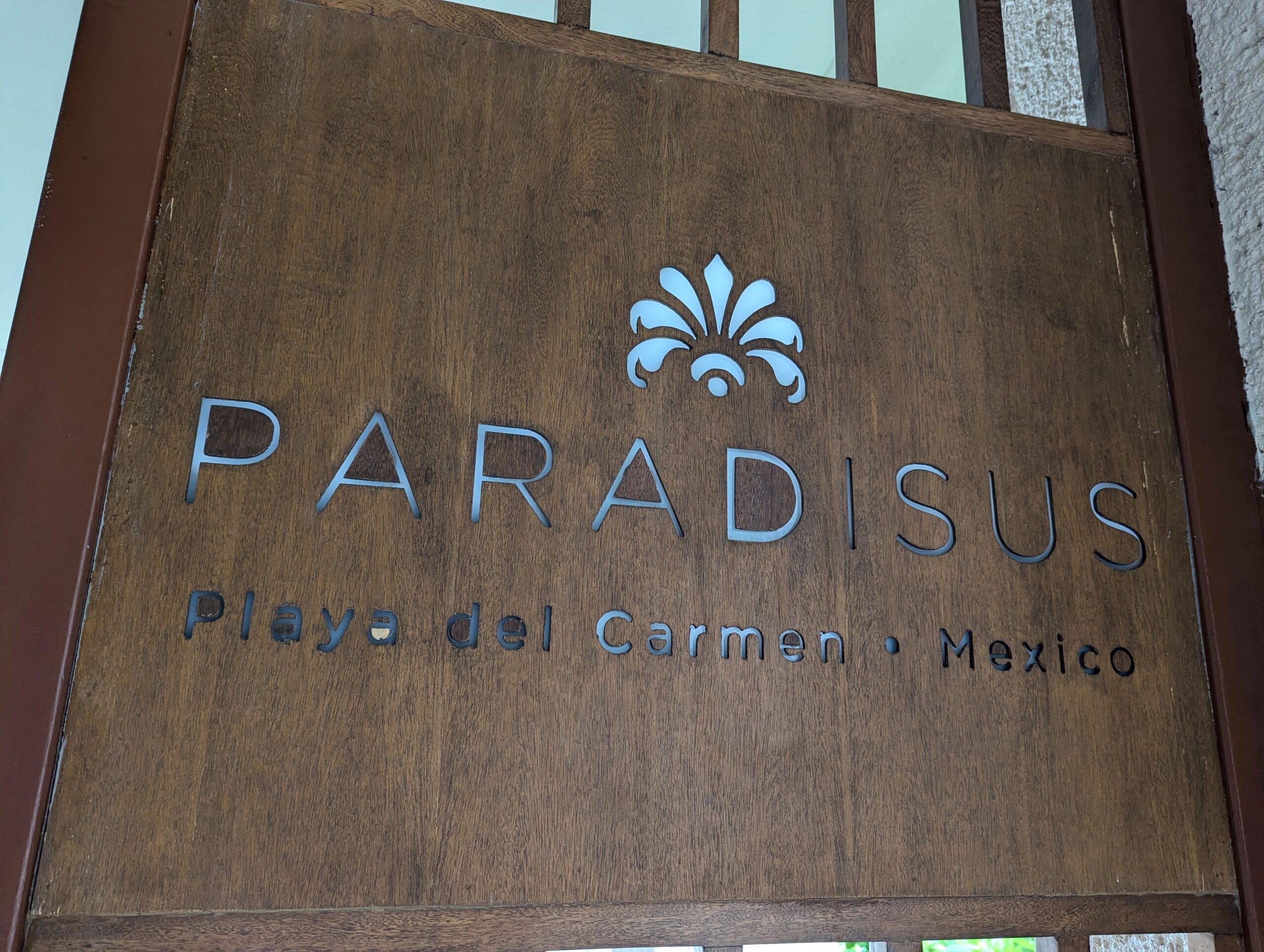 Close-up of a wooden sign for Paradisus La Perla All-Inclusive Resort, featuring engraved lettering