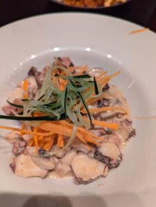 Close-up of a beautifully plated smoked octopus dish, garnished with fresh herbs and vegetables.