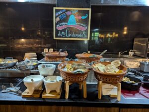 Chilaquiles station at a resort buffet featuring a variety of toppings and sauces, with a chef preparing fresh plates for guests.