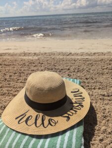 A straw hat resting on pristine white sand with the ocean waves gently lapping in the background on a sunny beach day.