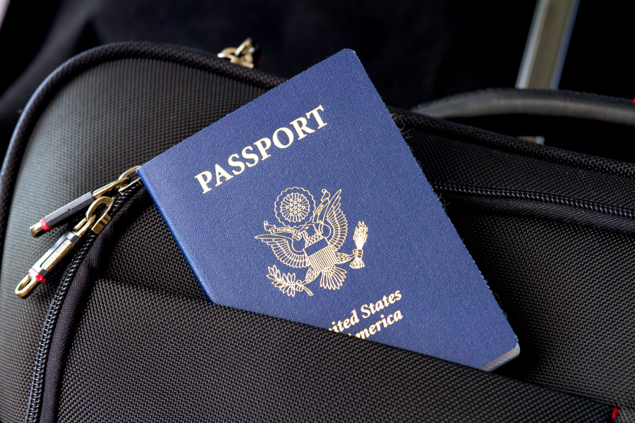 A passport partially visible, peeking out of the front pocket of a sleek black travel bag.