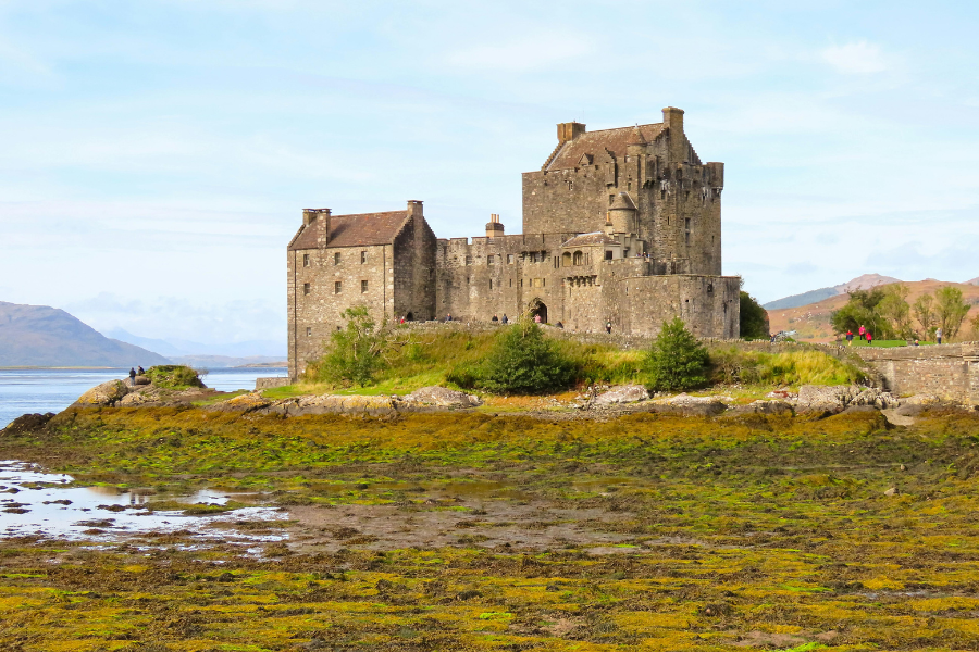 Majestic Eilean Donan Castle perched on a small tidal island at the confluence of three lochs, surrounded by serene waters and lush green hills under a partly cloudy sky in Scotland
