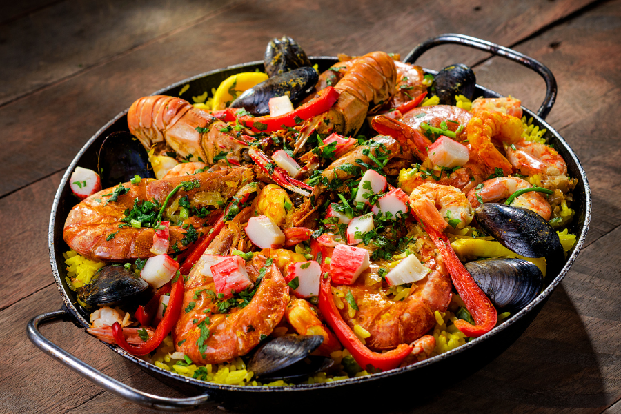 A vibrant dish of traditional Spanish paella, featuring saffron-infused rice, succulent shrimp, mussels, and colorful bell peppers garnished with fresh parsley.