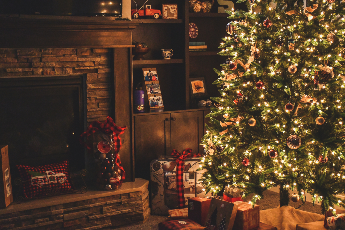 Cozy living room with a decorated Christmas tree beside a fireplace, styled in warm brown and neutral tones.