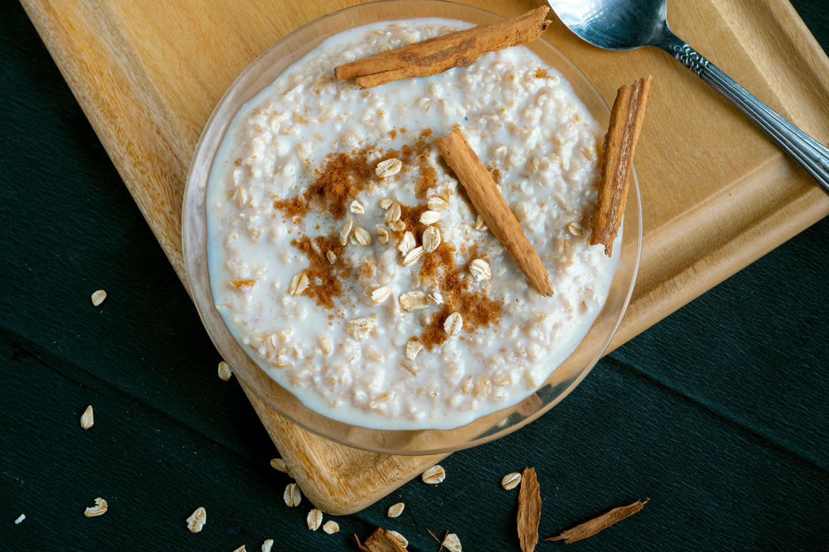 Bowl of creamy Christmas porridge topped with cinnamon and sugar, with cinnamon sticks on the side.