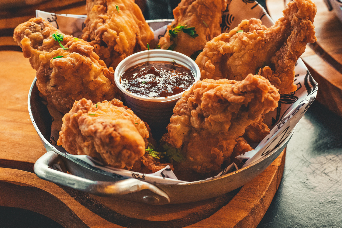 Fried chicken pieces in a metal bowl served with a small dish of dipping sauce on the side.