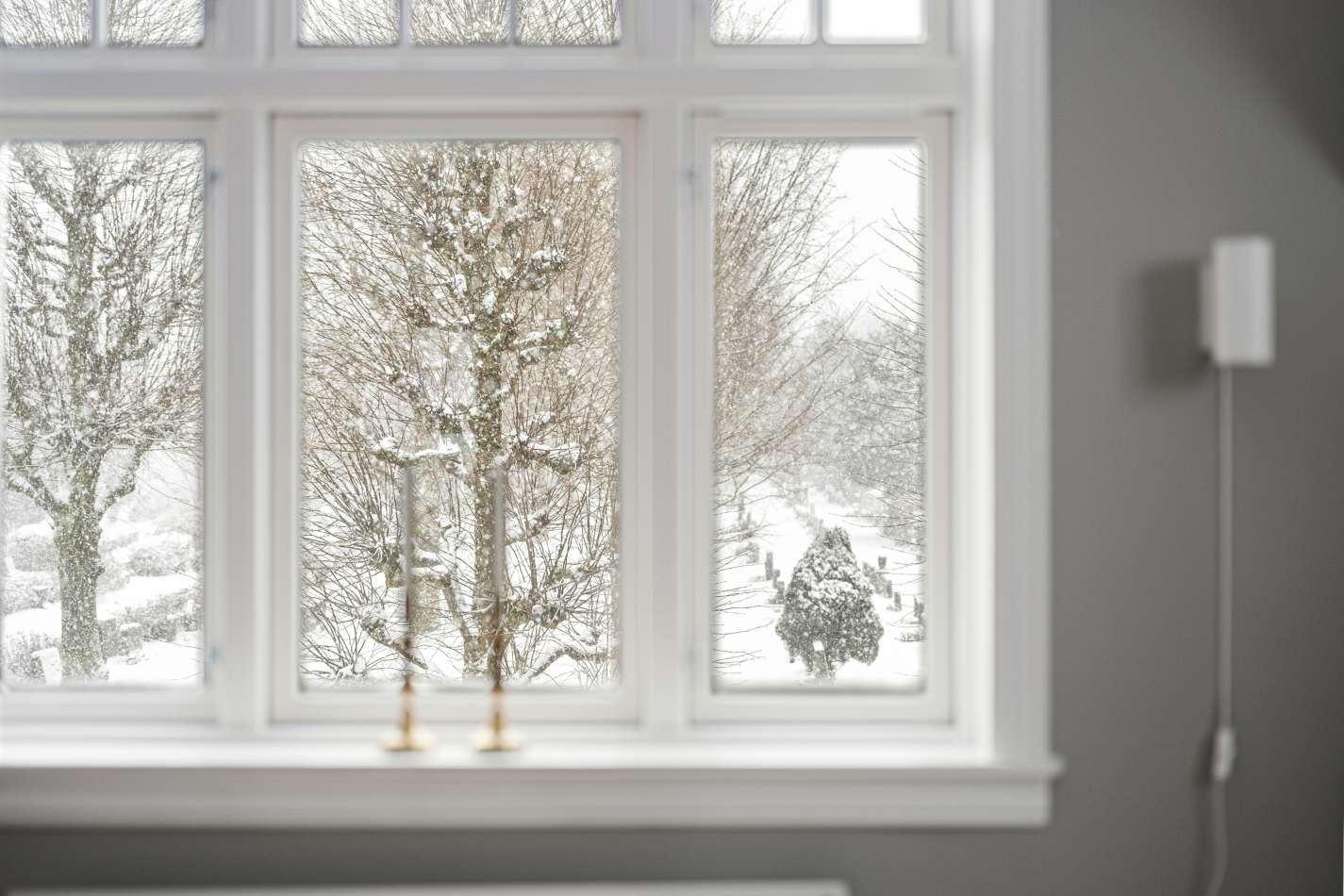 White window frame looking out onto a snowy winter landscape with snow-covered trees.