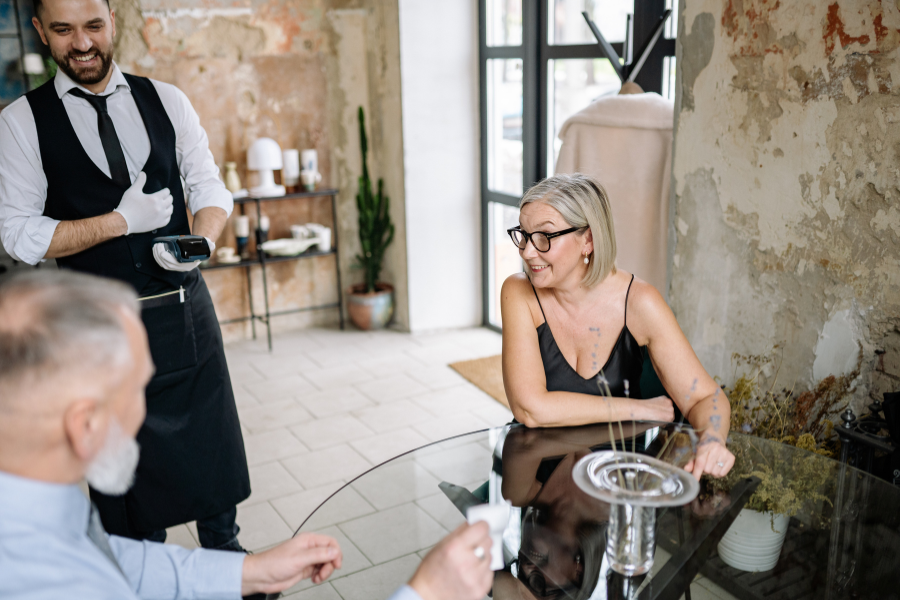 Man and woman at a restaurant handing a bank card to a waiter to pay their bill.